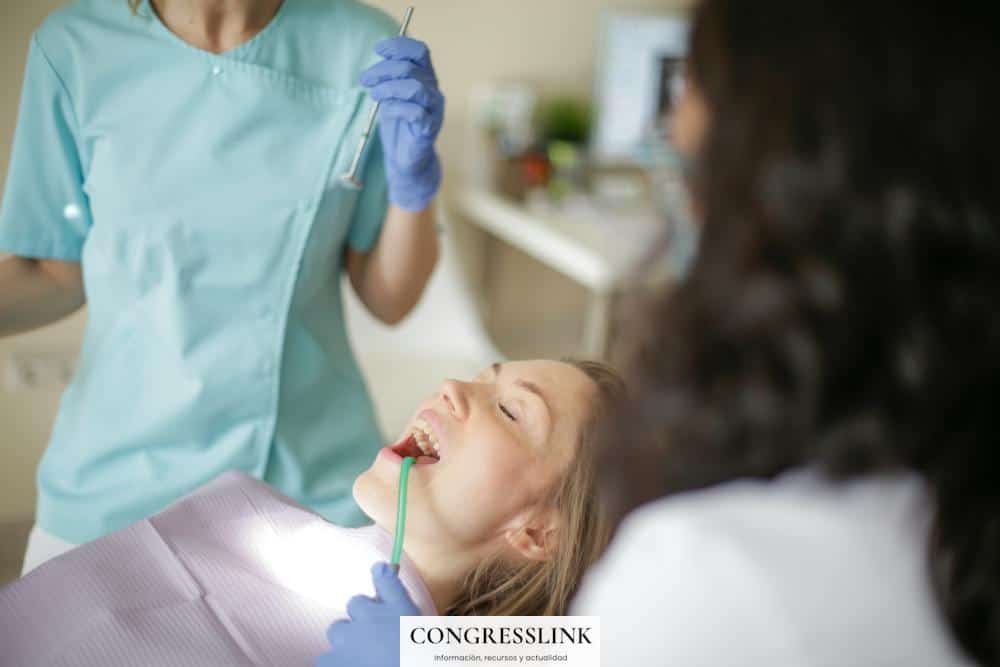 Crop faceless female dentist in uniform holding mouth mirror while preparing for inspecting female patient teeth with assistant holding tube suction in patient mouth